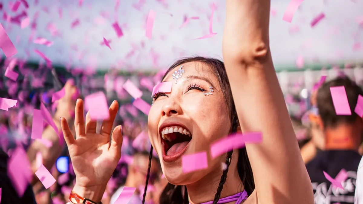 Jovem de braços erguidos comemorando no meio de uma chuva de confete rosa