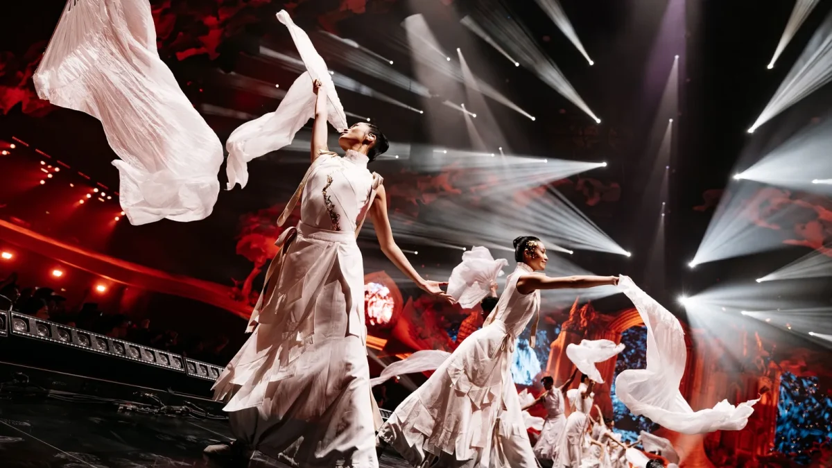 Bailarinas de branco girando leques de tecido em um palco iluminado de vermelho