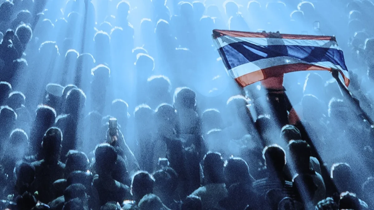 Bandeira da Tailândia erguida no meio do público, sob feixes de luz azul