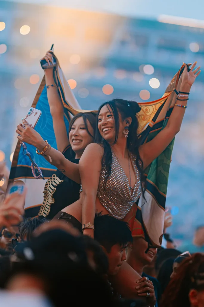 Duas pessoas erguidas nos ombros do público segurando uma bandeira, sorrindo
