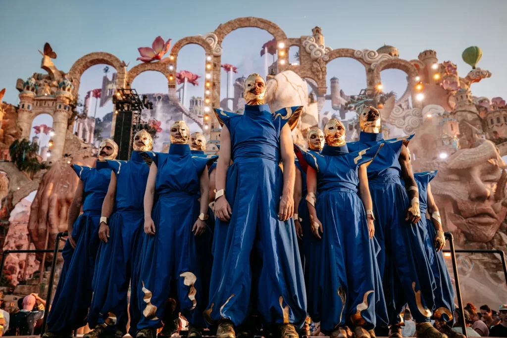 Bailarinos vestidos de azul com máscaras douradas em frente ao mainstage